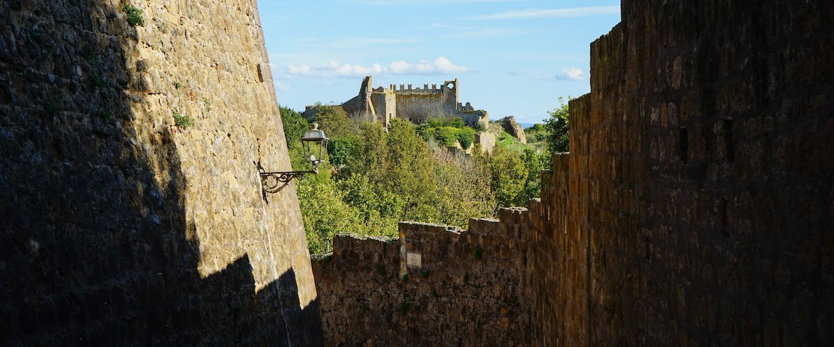A stone wall with a street lamp and a distant castle.