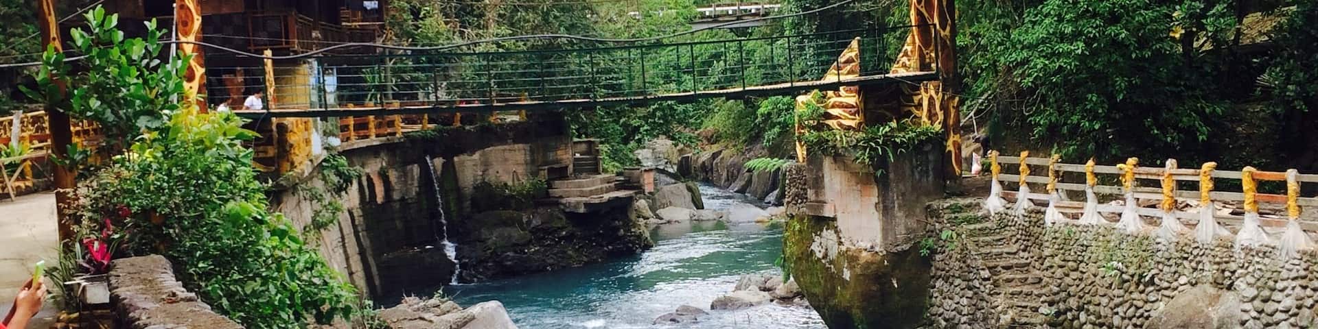 A river flowing through a rocky landscape with a wooden bridge and a building with a red roof.