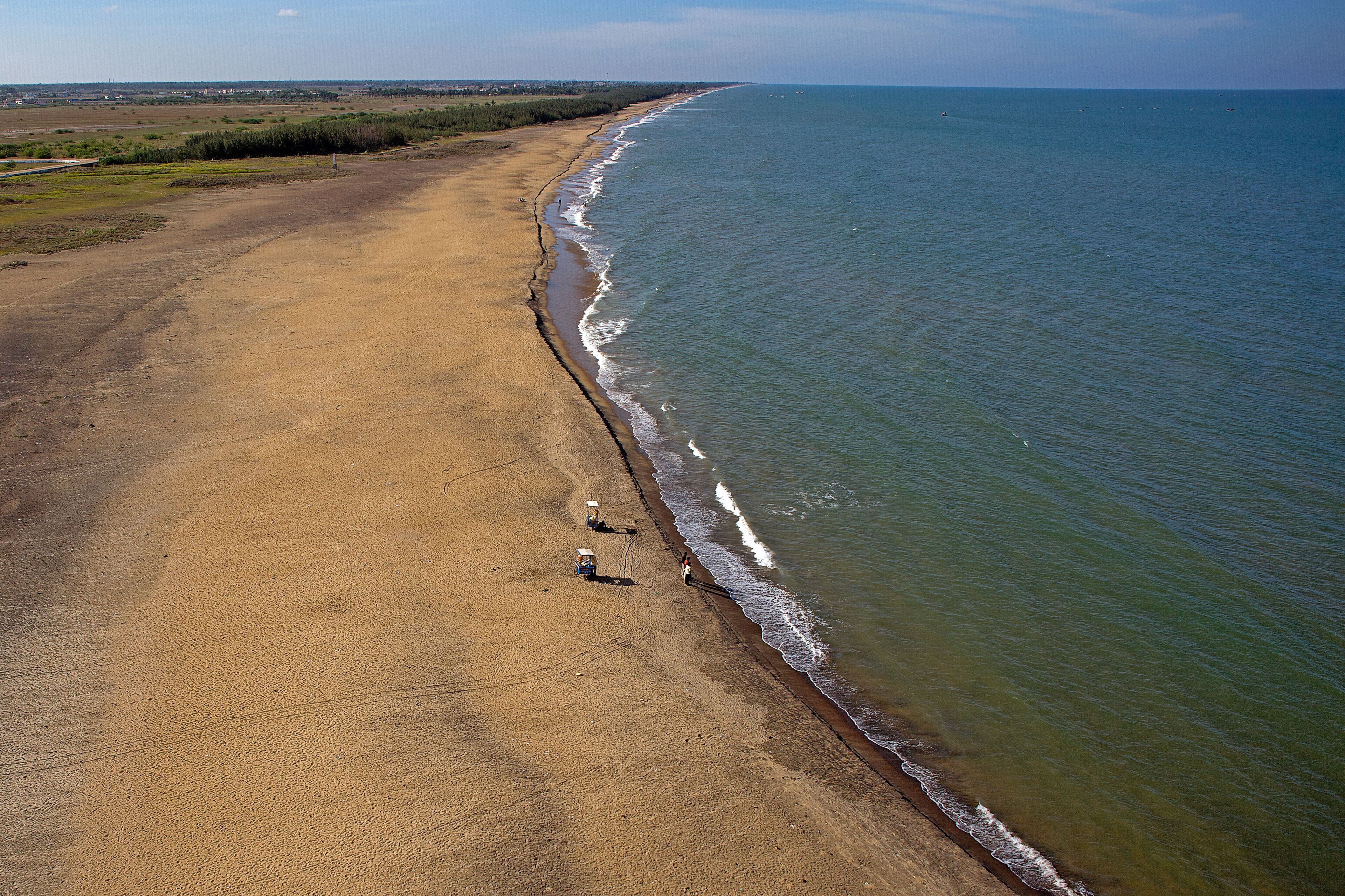 Aerial view of the golden sandy beach meeting the turquoise sea with gentle waves under a vast sky, Karaikal, Puducherry, India.