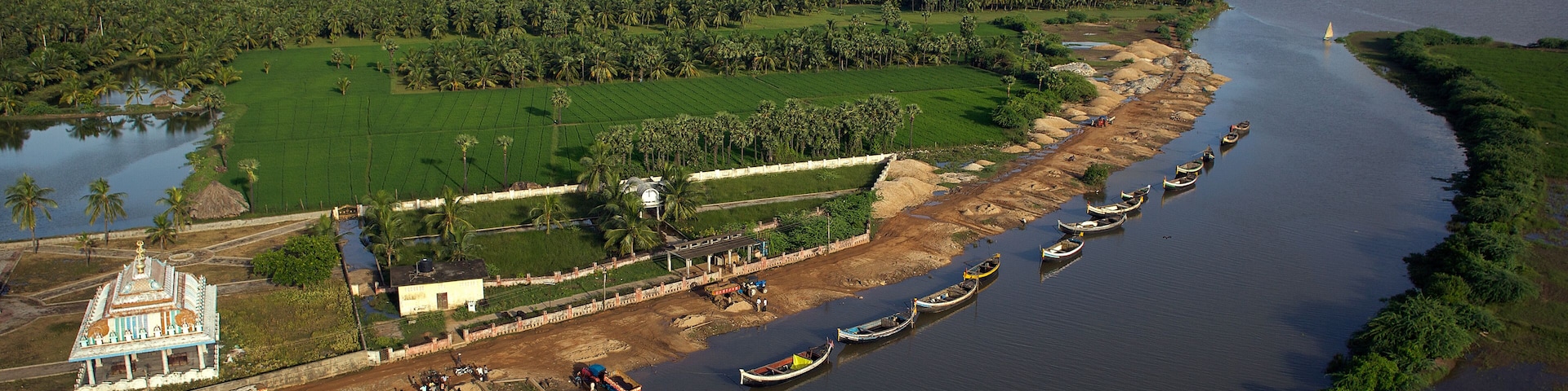 Yanam, India - 03 October 2010: Aerial view of the serene Godavari River winding past the vibrant green fields and boats docked along the shore near the temple.