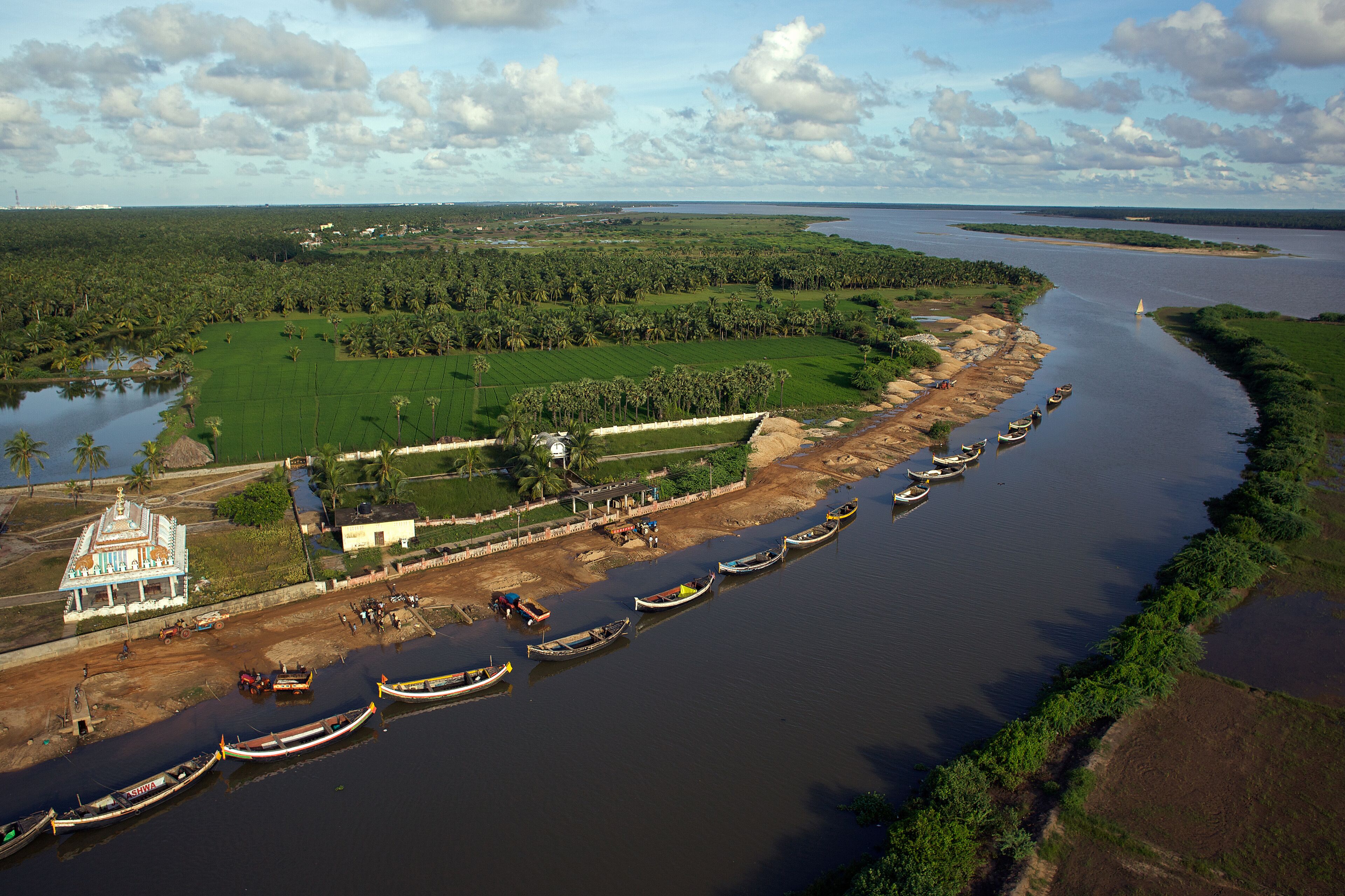 A river with boats, a temple, and surrounding greenery.