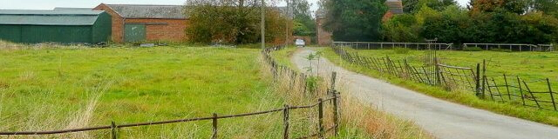 Un camino rural serpentea a través de campos, con un granero y una cerca a la izquierda.