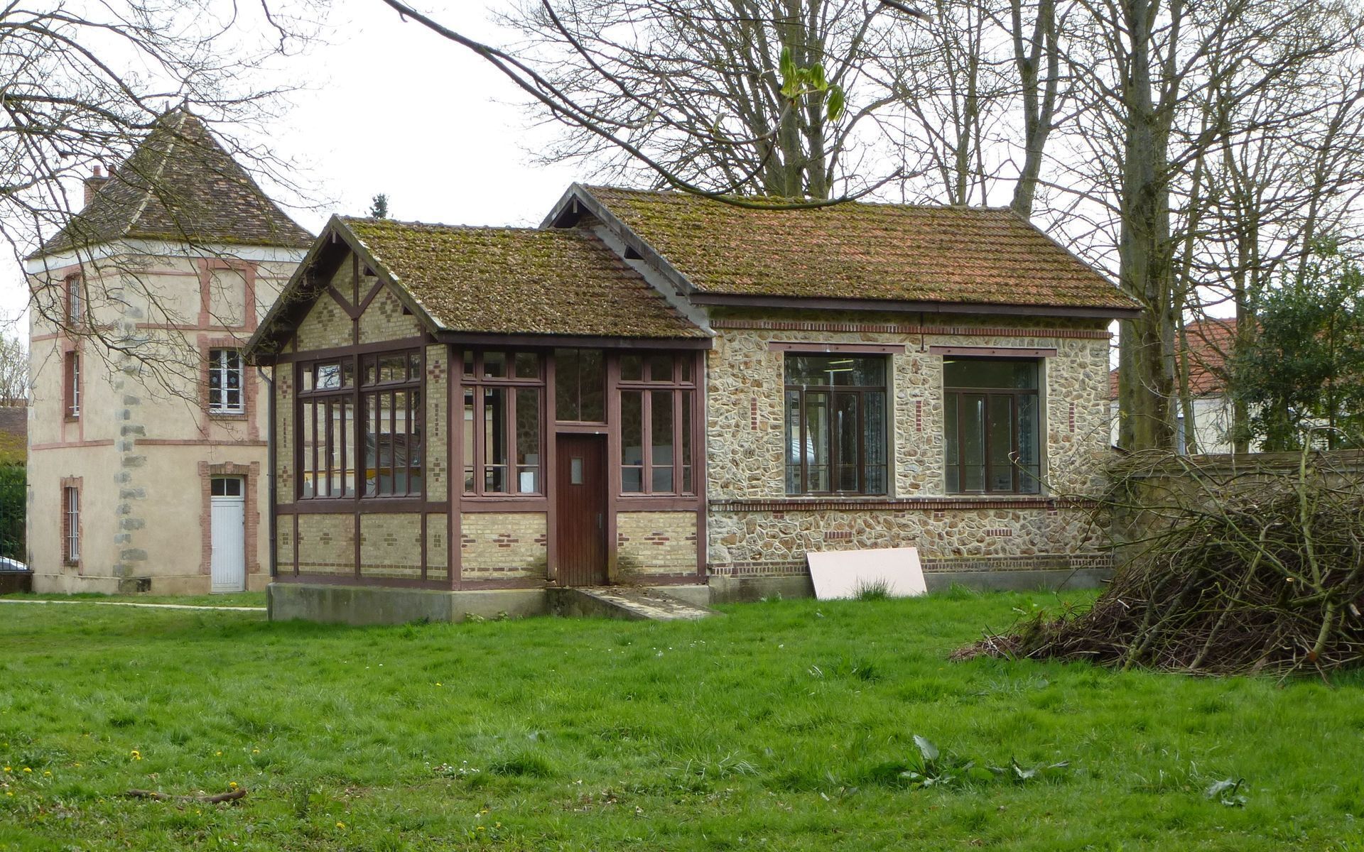 A traditional stone and timber house with a steeply pitched roof, a small tower, and a grassy yard.