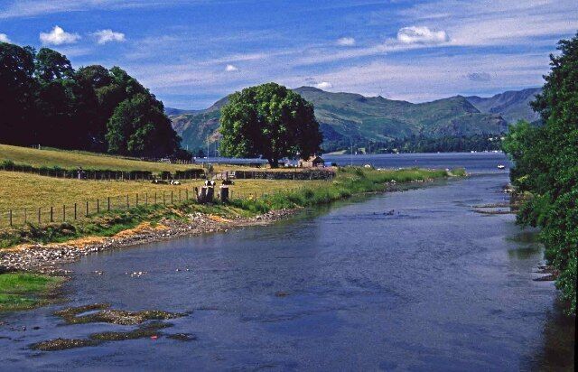 A river with a fence, trees, and mountains in the background.