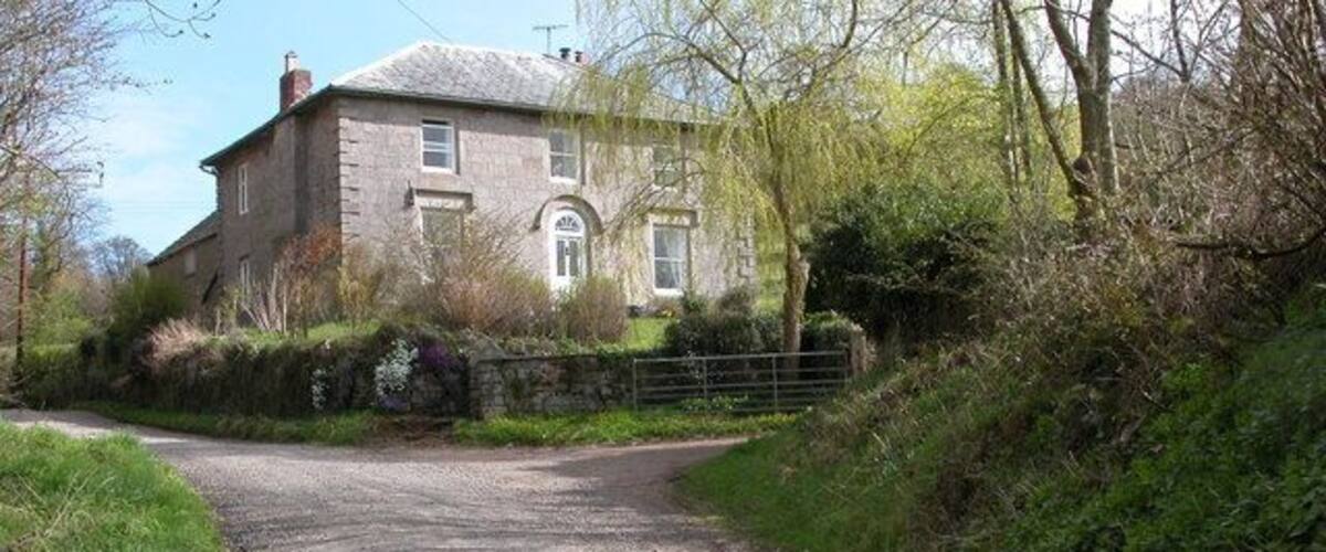 A rural road leading to a stone house surrounded by greenery.