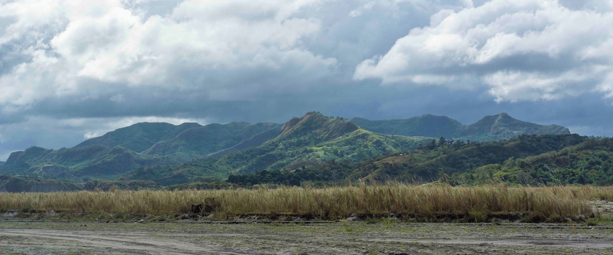 A landscape with rolling hills, a grassy foreground, and a cloudy sky.