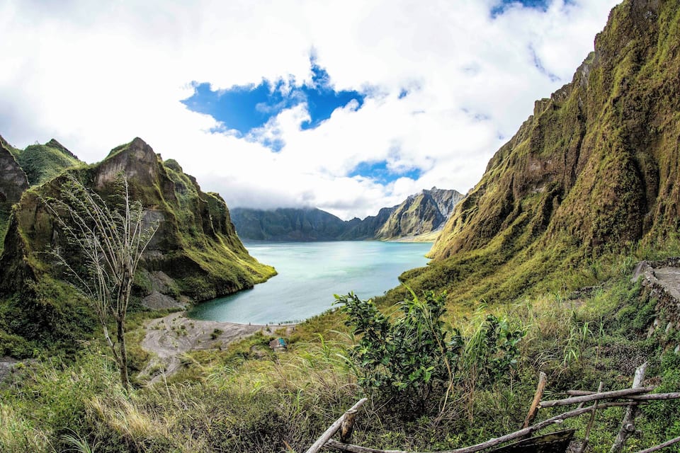 A mountainous landscape with a turquoise lake surrounded by lush greenery and rocky cliffs.
