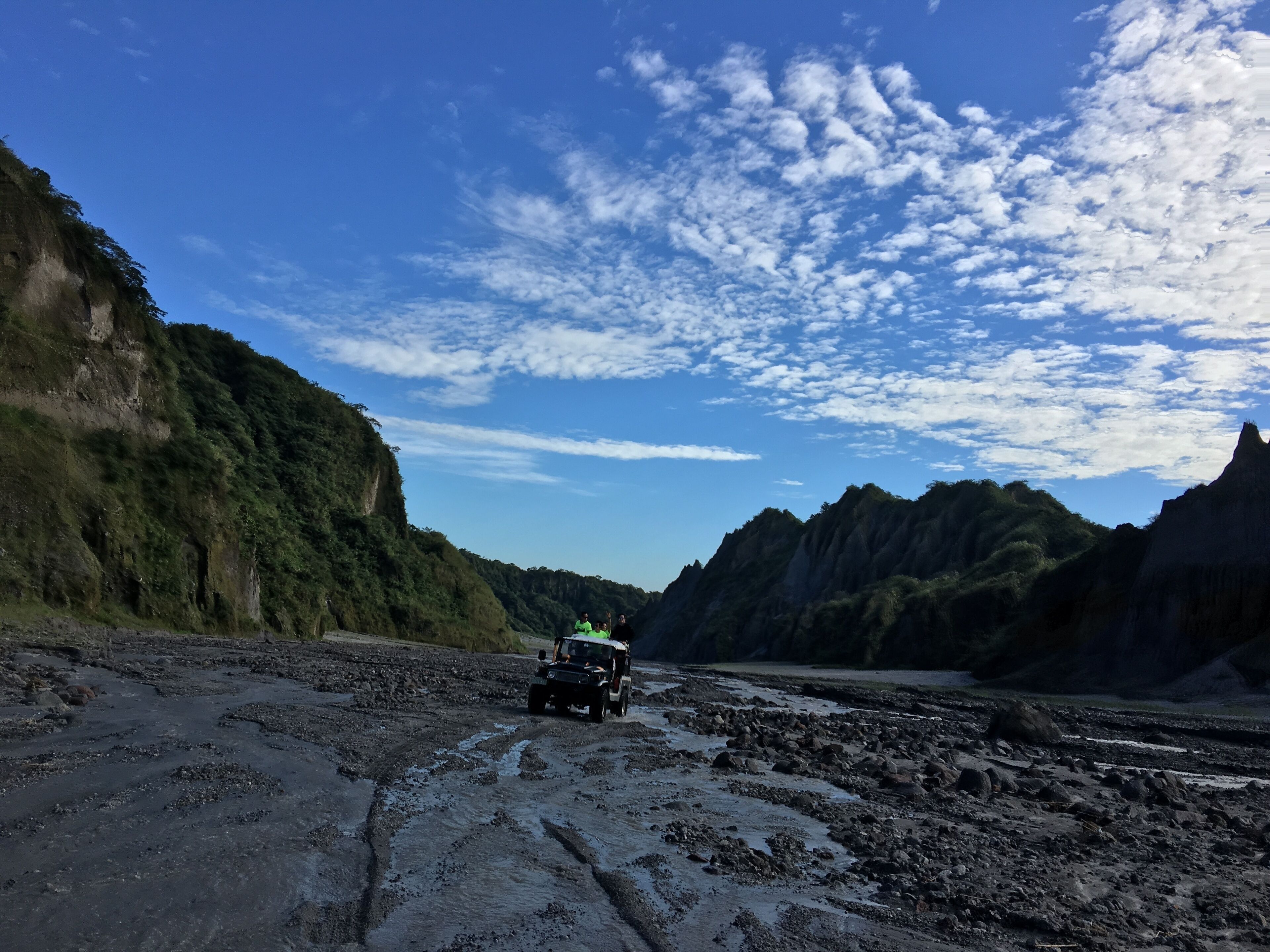 A jeep on a muddy path with mountains in the background.