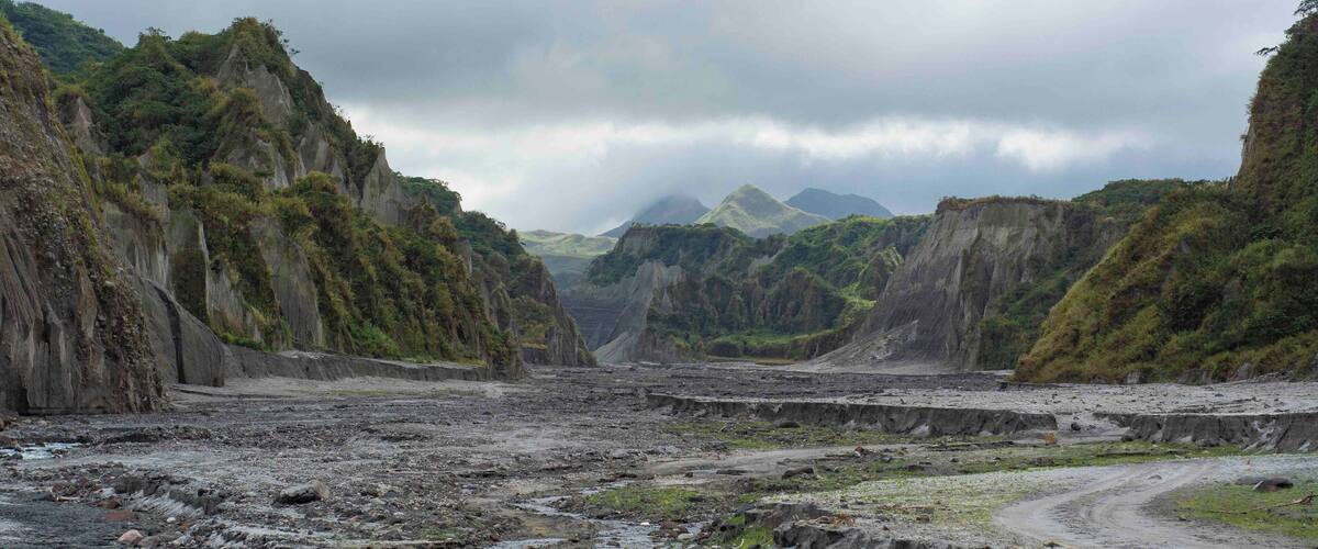 Un paisaje agreste con acantilados escarpados, un camino serpenteante y montañas distantes bajo un cielo nublado.