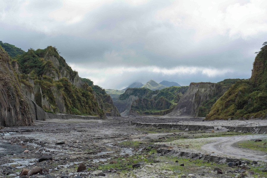 Un paisaje agreste con acantilados escarpados, un camino serpenteante y montañas distantes bajo un cielo nublado.