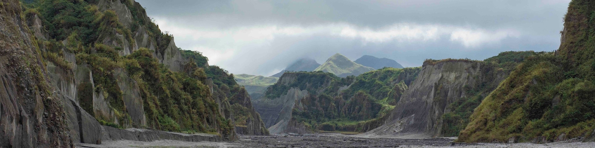 Un paisaje agreste con acantilados escarpados, un camino serpenteante y montañas distantes bajo un cielo nublado.