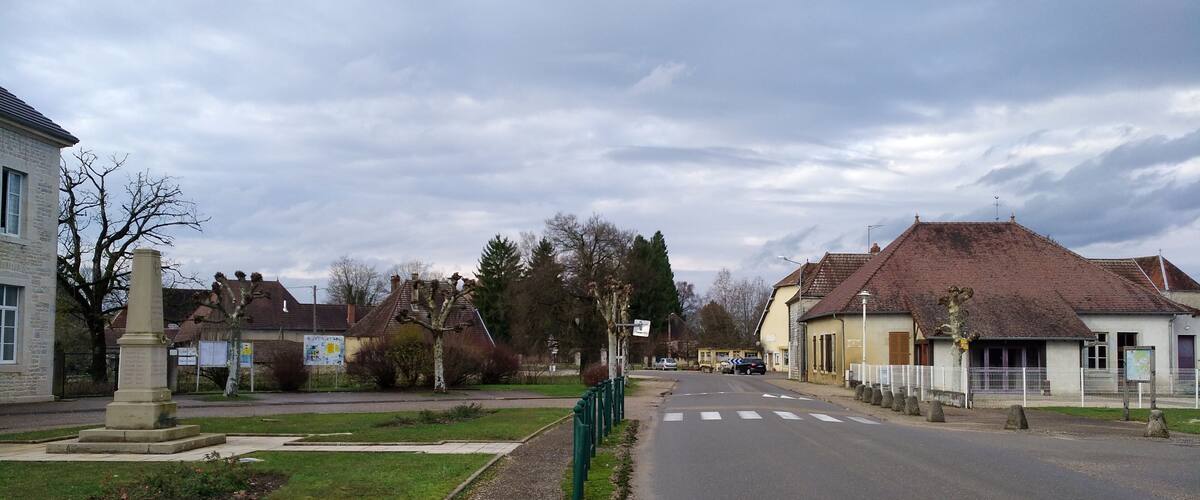 A quiet residential street with houses, a monument, and a grassy area.