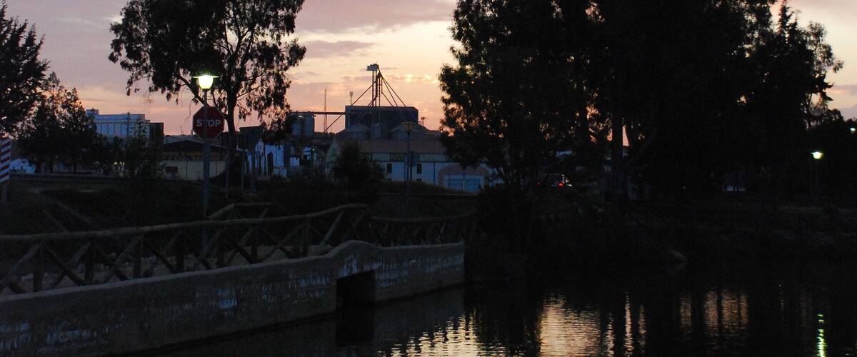 A sunset over a calm river with trees and a bridge.