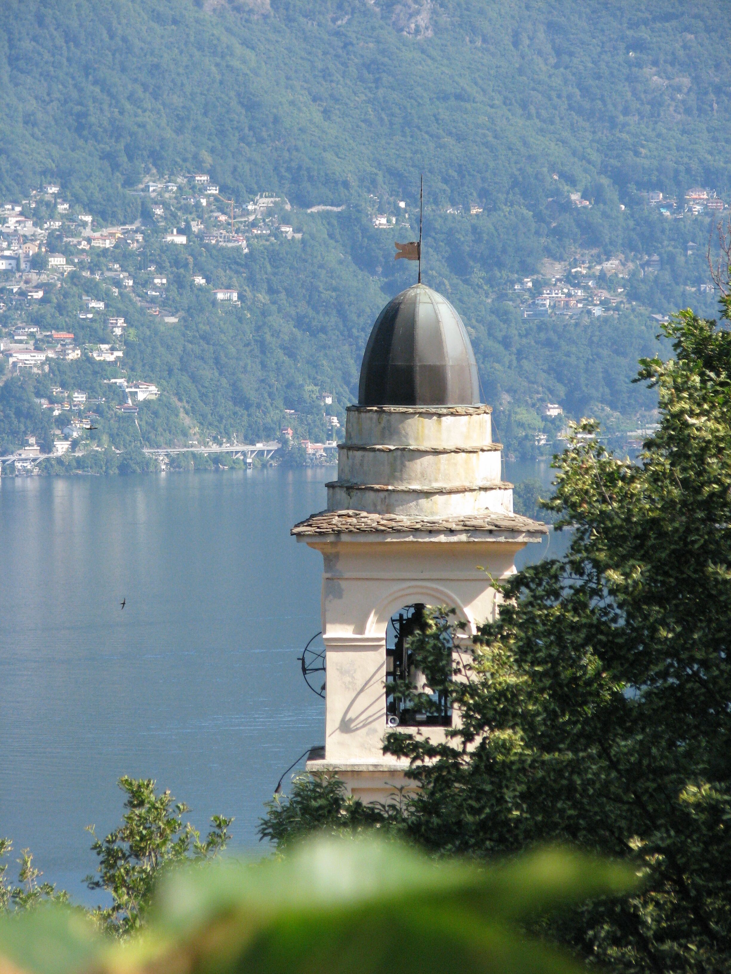 A tower with a dome and flag, overlooking a lake with a mountainous backdrop.