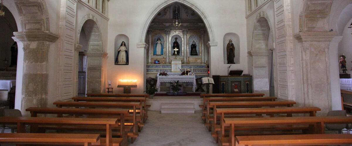 An interior of a church with wooden pews, a central altar, and statues on either side.