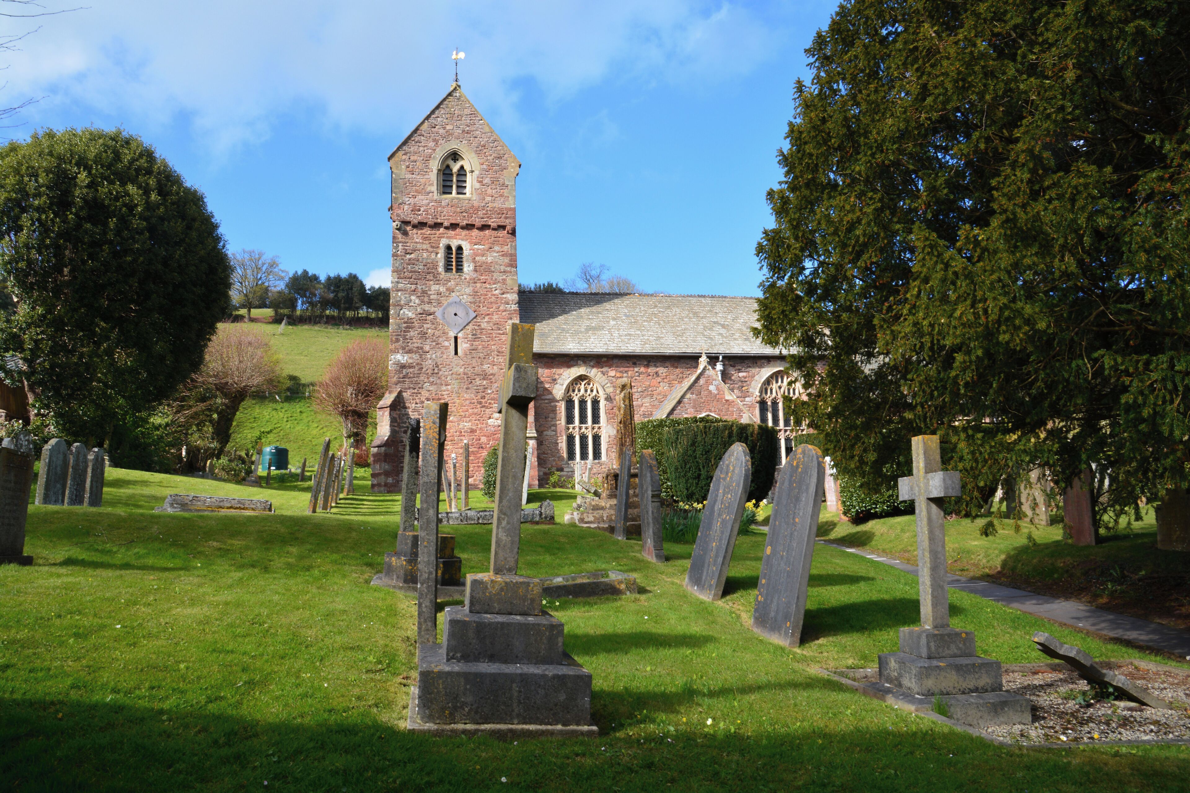 A church with a tall tower and a cemetery with numerous gravestones.