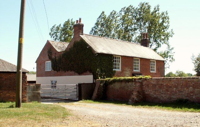 A traditional brick house with a sloped roof and ivy-covered walls, a gravel driveway, and a metal gate.