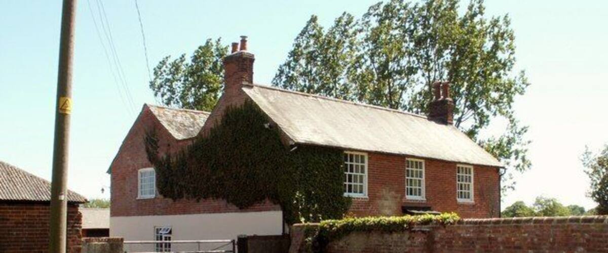 A traditional brick house with a sloped roof and ivy-covered walls, a gravel driveway, and a metal gate.
