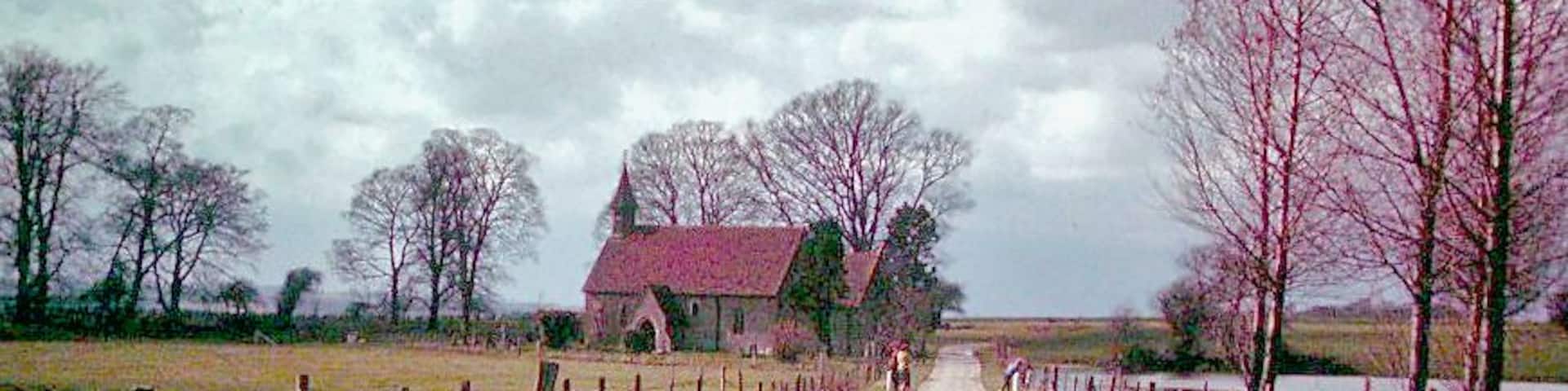 A rural road with a red-roofed building, a fence, and bare trees.