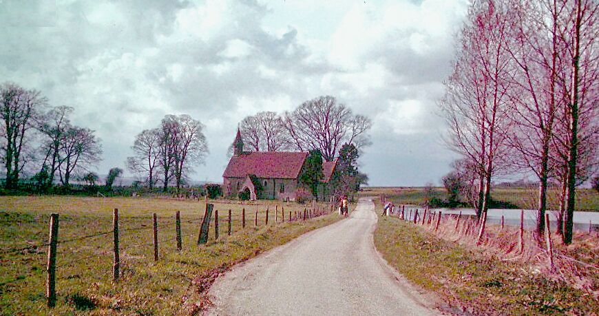 A rural road with a red-roofed building, a fence, and bare trees.