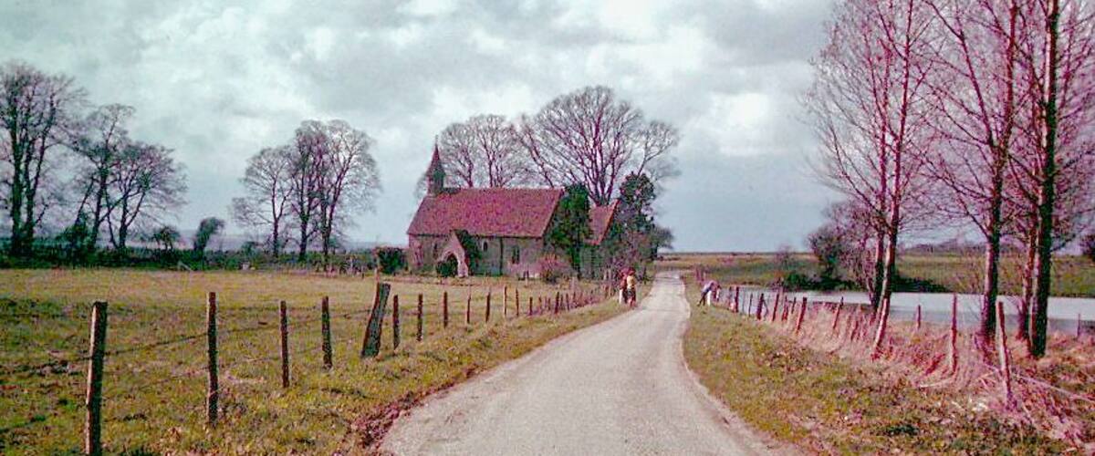 A rural road with a red-roofed building, a fence, and bare trees.