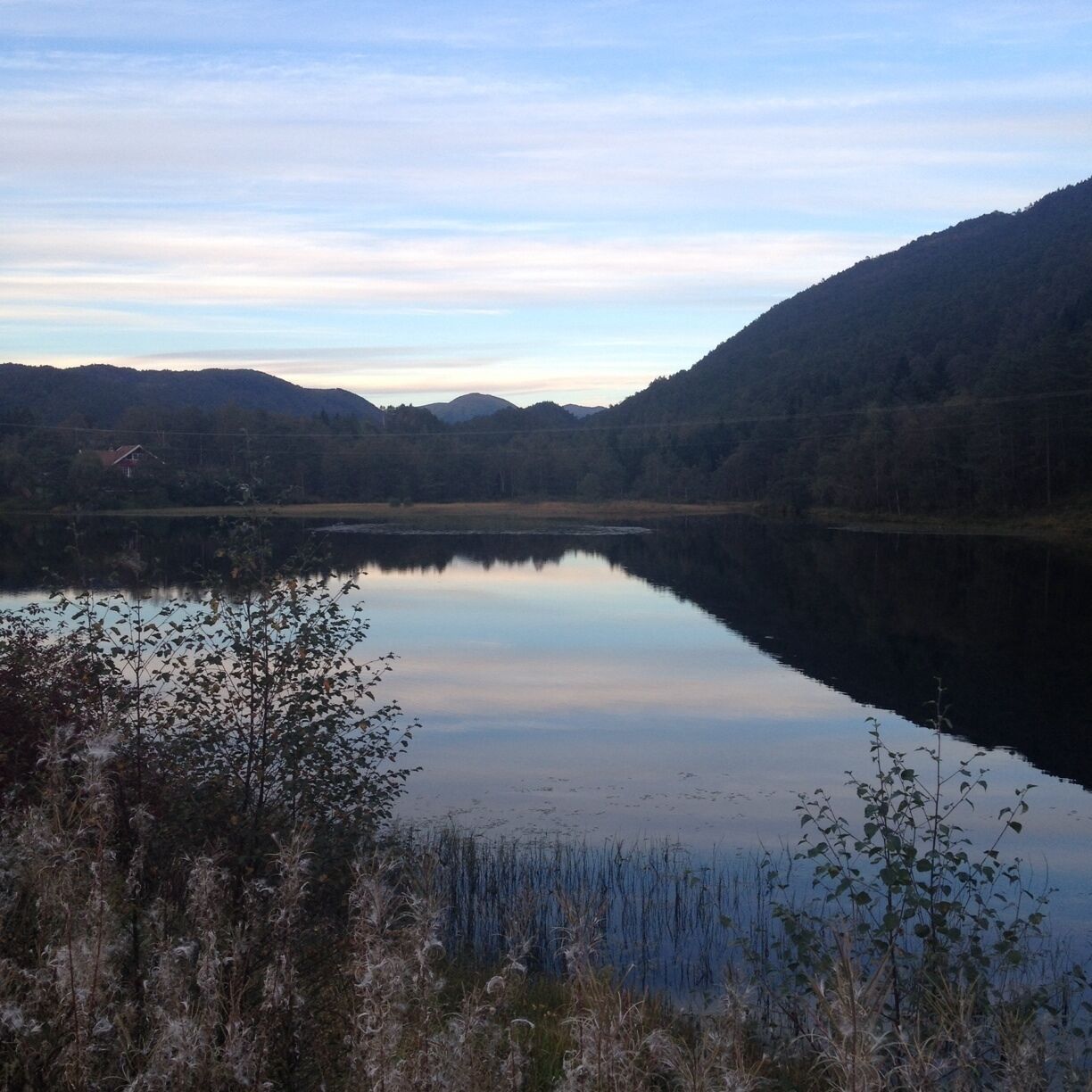 A calm lake surrounded by mountains and sparse vegetation.
