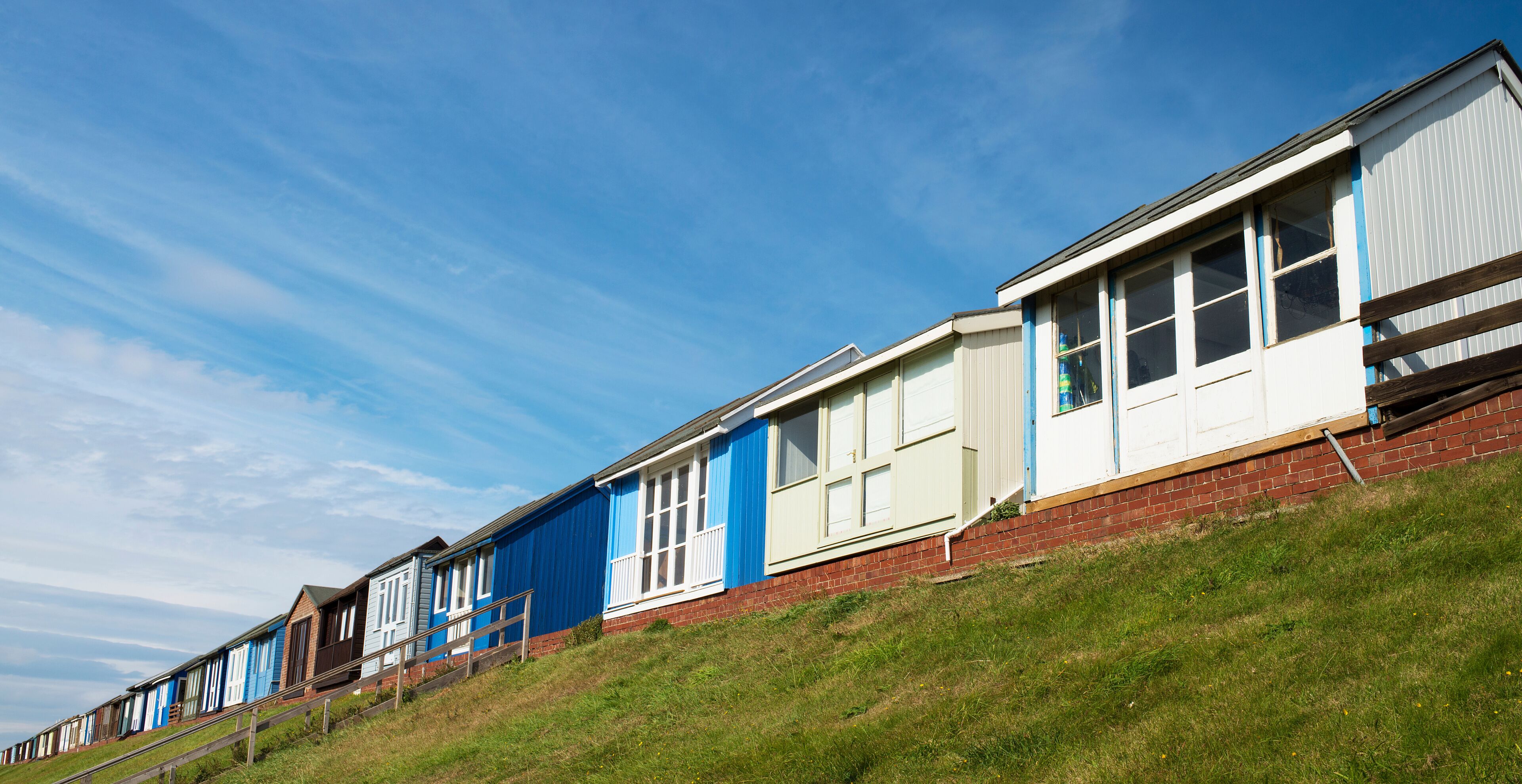 A row of beach huts with blue and white exteriors, set against a clear blue sky.