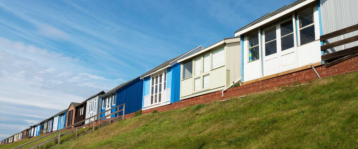 A row of beach huts with blue and white exteriors, set against a clear blue sky.