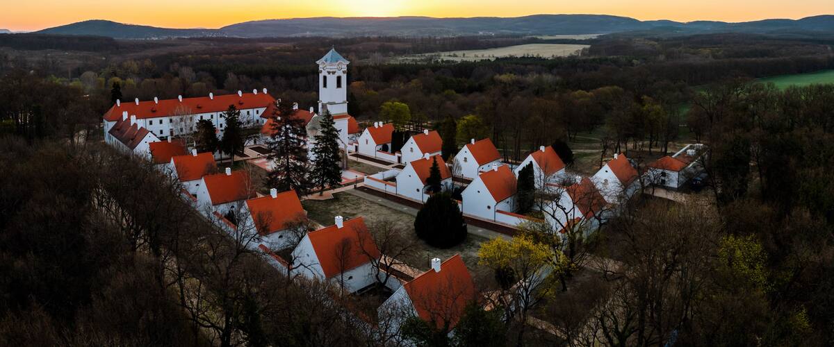 A village with white buildings and red roofs, surrounded by trees and hills.