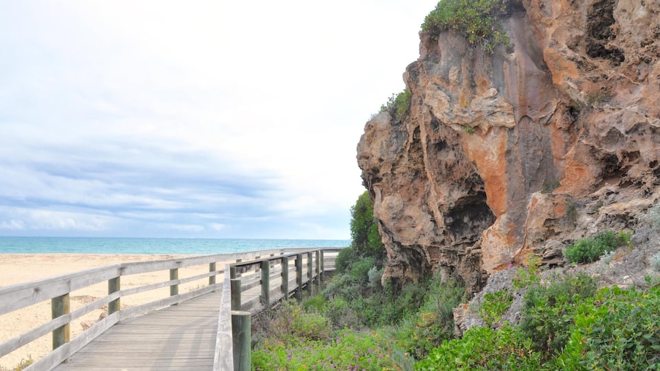 A wooden boardwalk leading to a beach with a rocky cliff in the background.