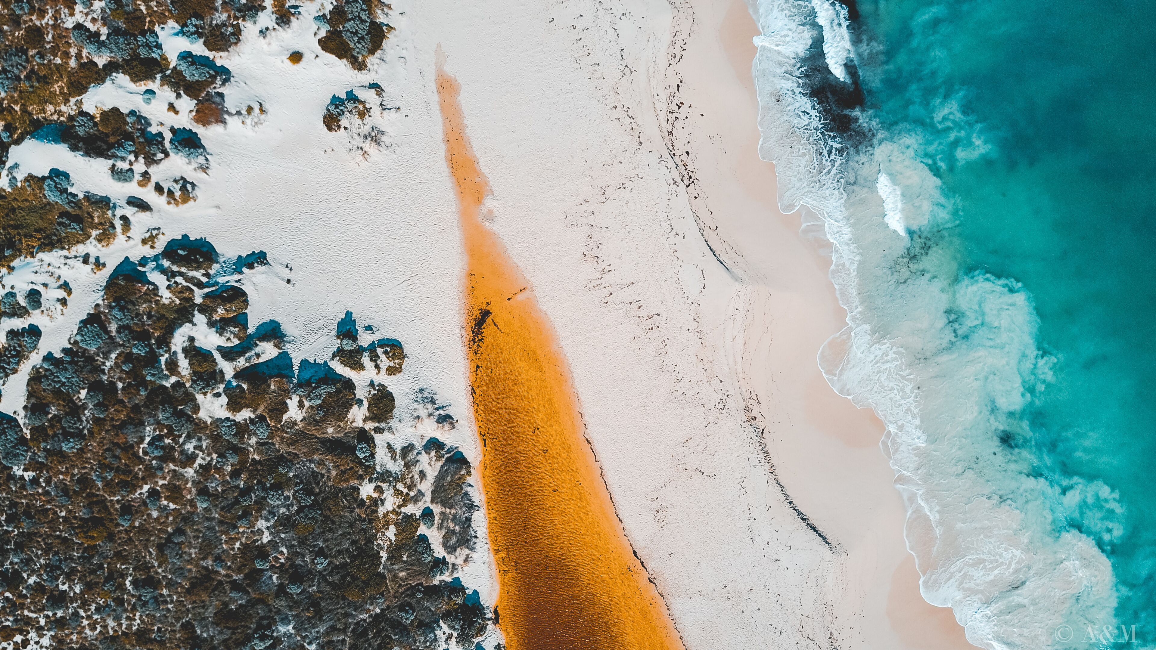Aerial view of where the river meets the sea. Vibrant orange and dark river meet turquoise sea waves on beach in Western Australian town called Guilderton.