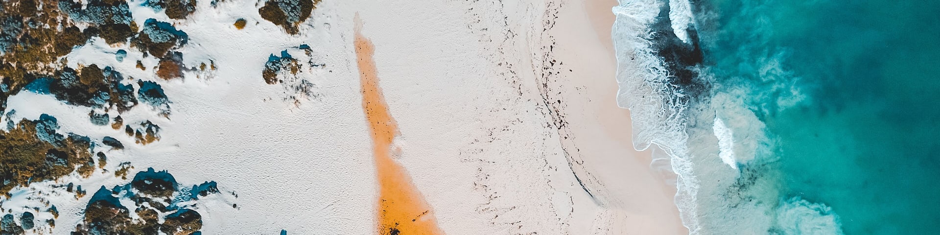 Aerial view of where the river meets the sea. Vibrant orange and dark river meet turquoise sea waves on beach in Western Australian town called Guilderton.