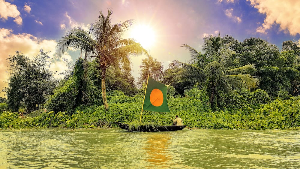 A fishermen fishing on a small boat collecting green plants and fishes for sell, from The Padma river in
Bangladesh.
Nice blue sky with clouds and bright sun shining across green beautiful forest.