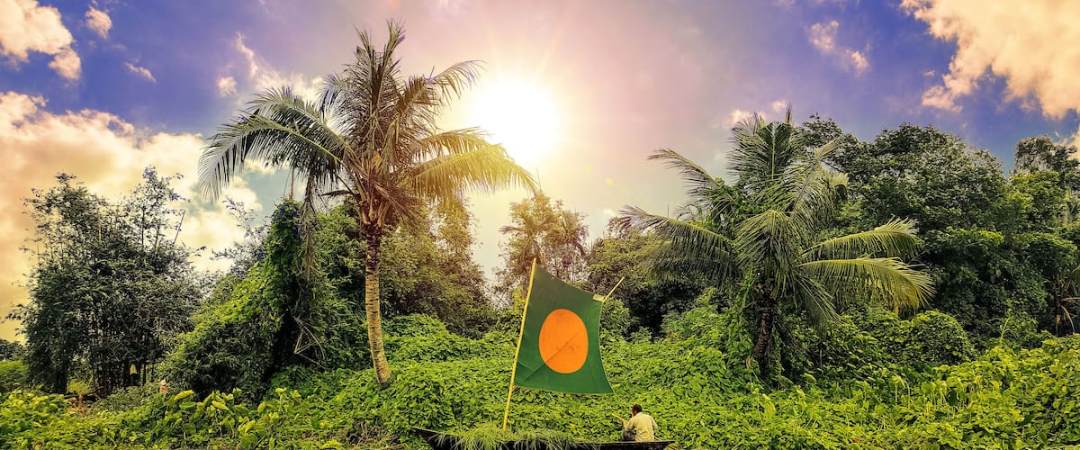 A boat with a flag on a river surrounded by dense greenery and palm trees.