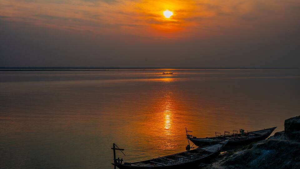 A sunset over a calm sea with boats docked on a rocky shore.