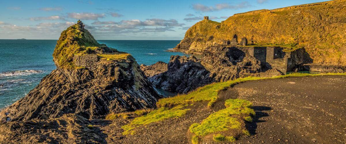 A coastal landscape with rocky cliffs, a grassy path, and a small tower on a hill.