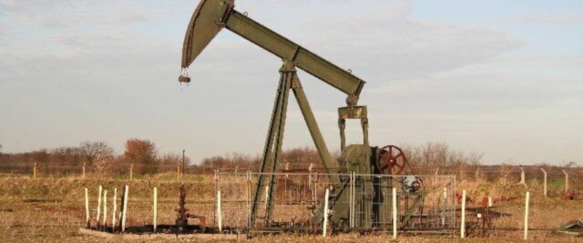 An oil pumpjack in a field with a fence around it.