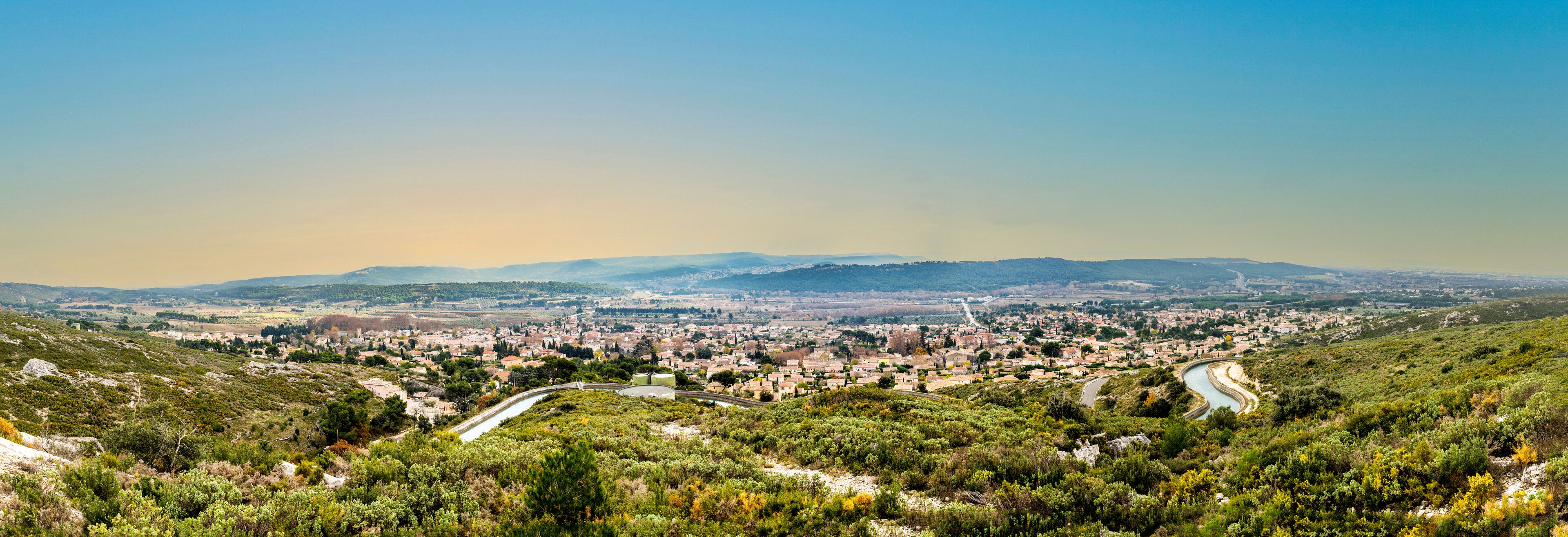 A town nestled in a valley with a river winding through it, surrounded by hills and greenery.