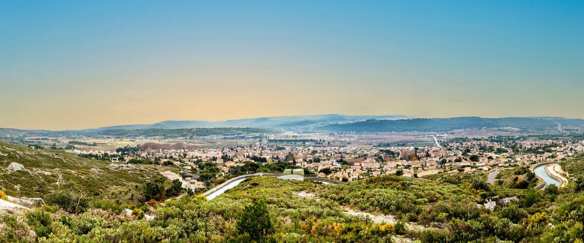 A town nestled in a valley with a river winding through it, surrounded by hills and greenery.