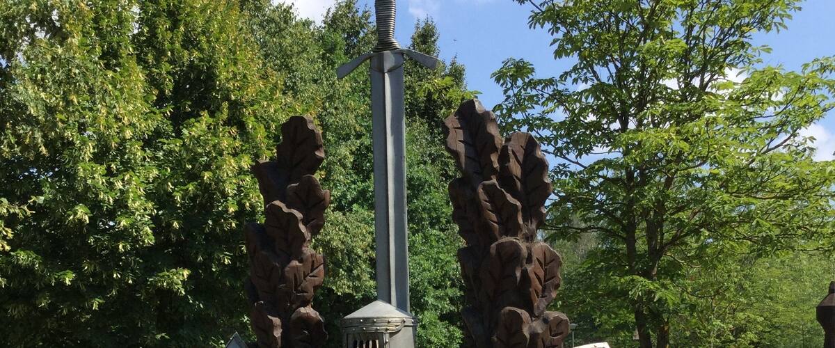 A monument with a sword and shields, labeled "ZAGGIRIS," in a park with trees and grass.