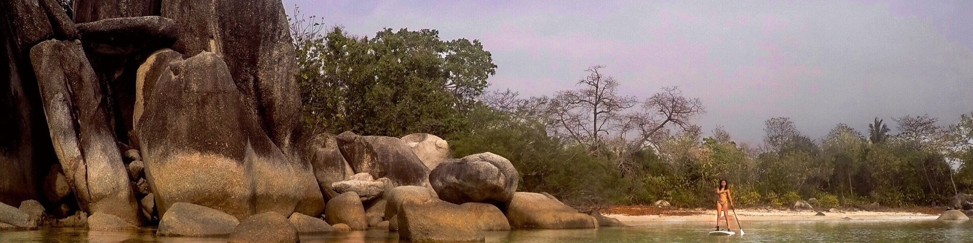 Un cuerpo de agua cristalina con rocas grandes y una persona haciendo paddleboard.