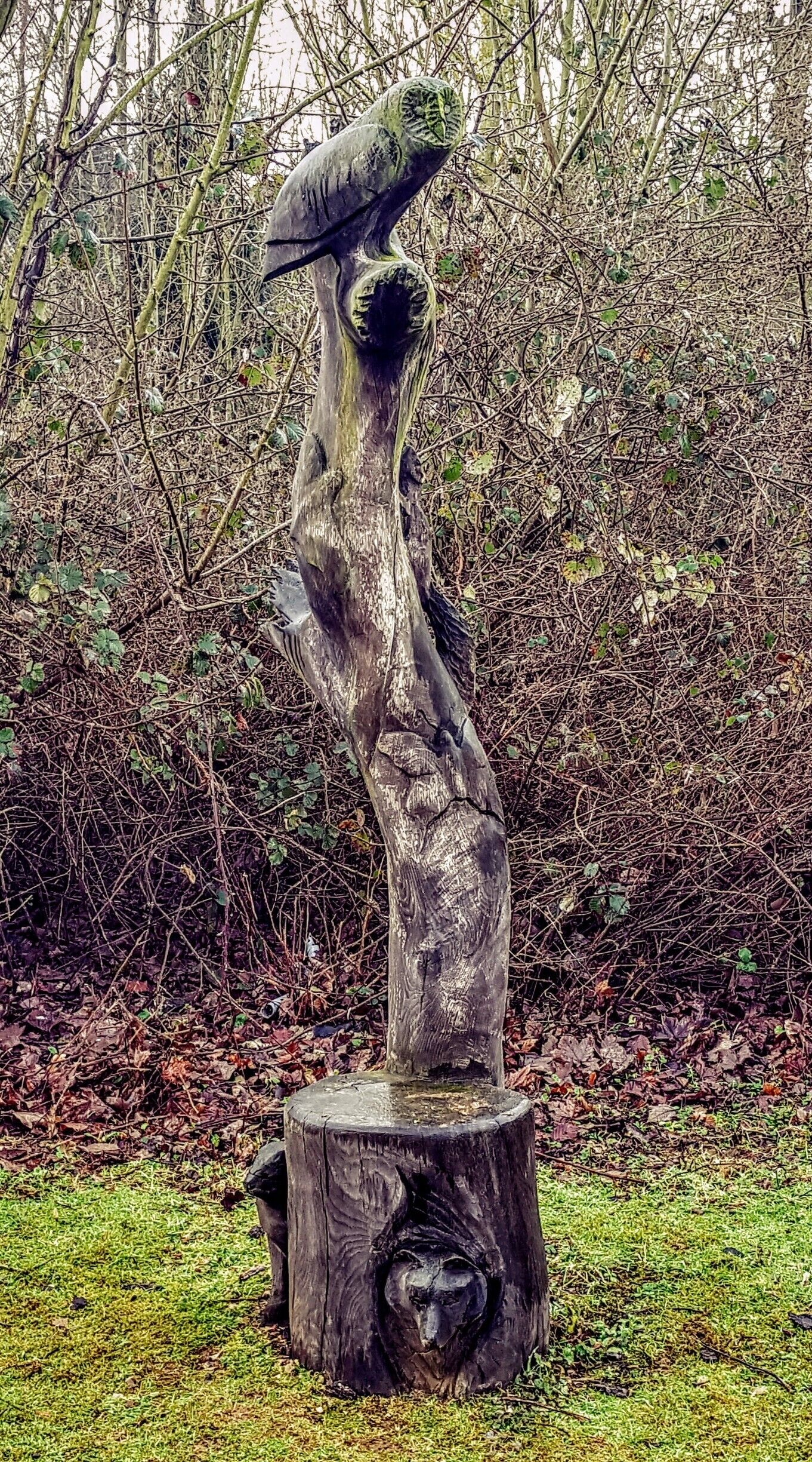 A wooden sculpture of a figure balancing a bowl on its head, set on a tree stump in a forested area.