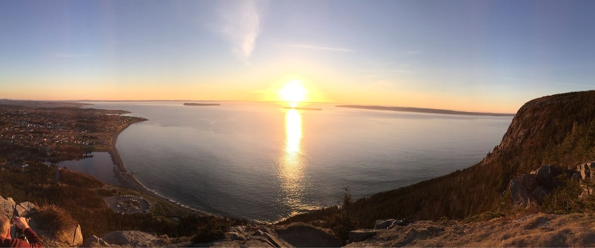A sunset over a large body of water with a city in the distance and a mountainous landscape in the foreground.