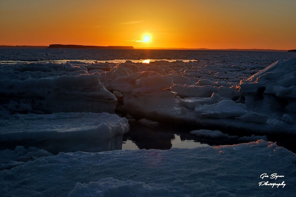 Atardecer sobre un paisaje congelado con formaciones de hielo y una pequeña masa de agua que refleja el sol.