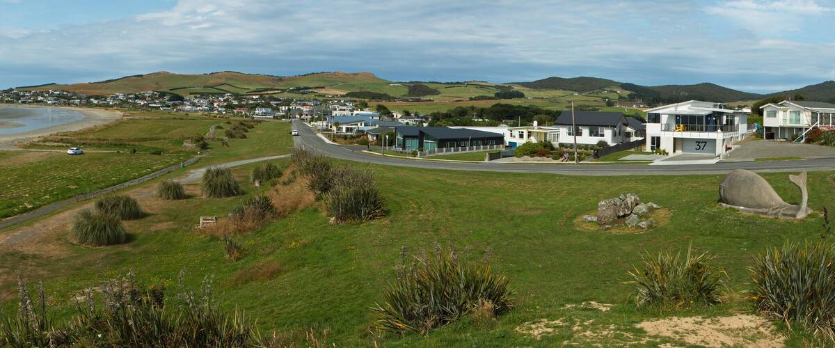 A coastal town with a beach, houses, and rolling hills in the background.