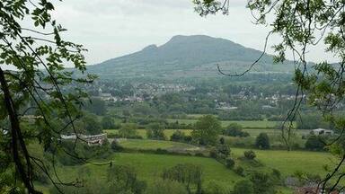 A lush green valley with rolling hills, a distant mountain, and a small town in the background.