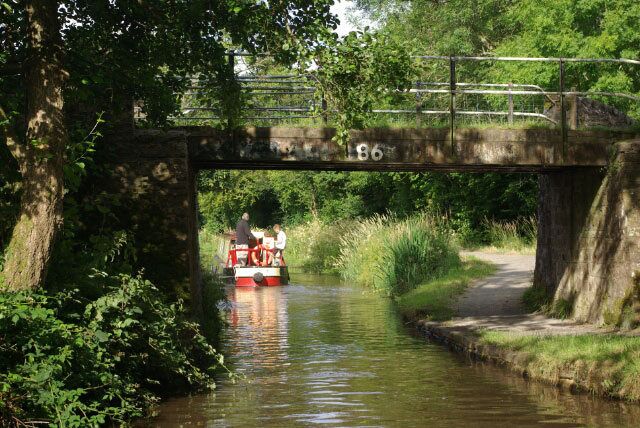 A narrow waterway with a red and white boat under a bridge marked with the number 86.
