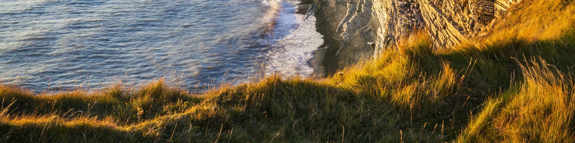 A coastal cliff with layered rock formations and a sandy beach.
