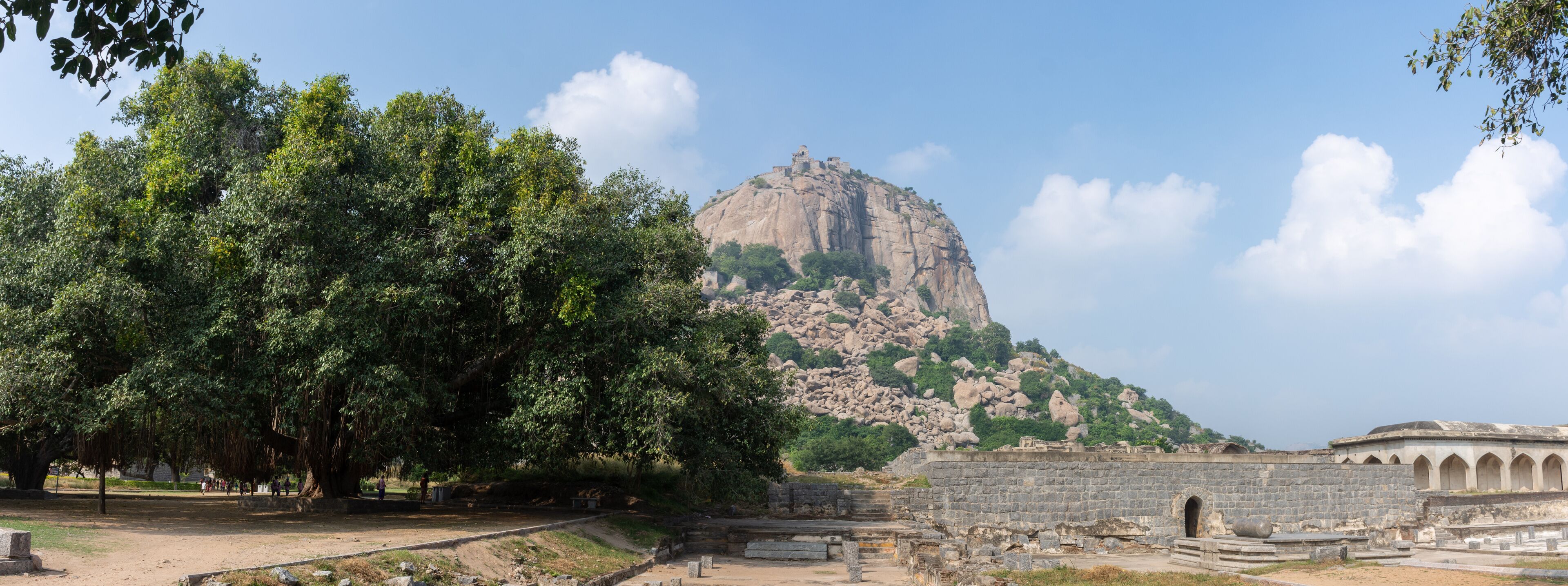 A large rock formation with ruins and trees.