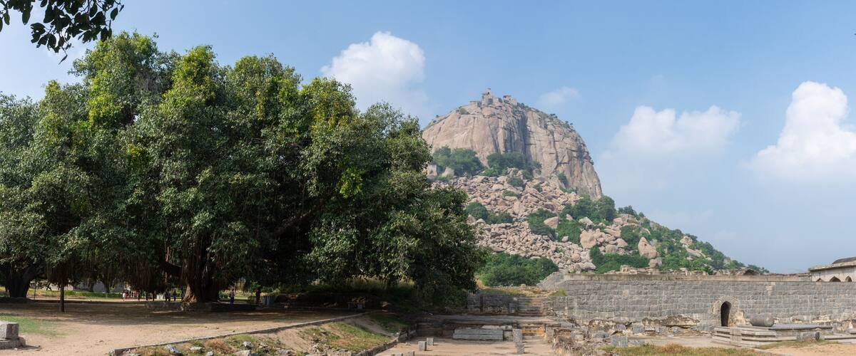 A large rock formation with ruins and trees.